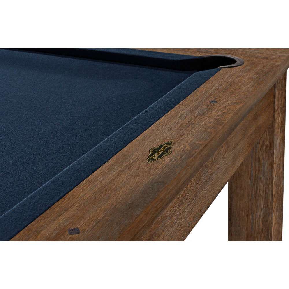 Gros plan sur une table de billard américain Soho d'Brunswick, dotée d'un tapis bleu foncé et d'un cadre en bois au fini noyer. Ce détail montre une poche d'angle et le logo ovale doré « Brunswick » sur la bande de cette élégante table.