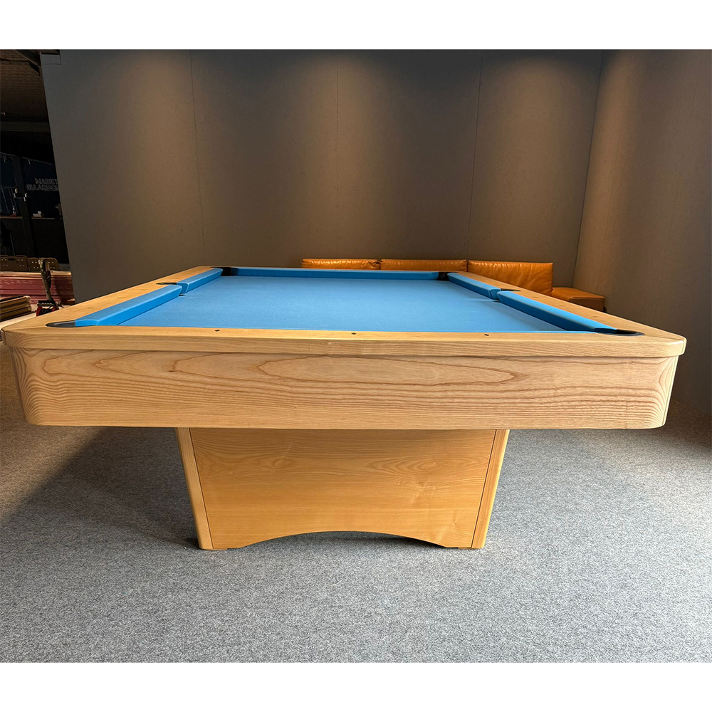 Élégante table de billard Kairos en bois massif clair aux veines apparentes. La surface de jeu bleue contraste avec les bandes arrondies sur tout le pourtour. Design épuré reposant sur un socle stable et légèrement incurvé. Repose sur un tapis gris.