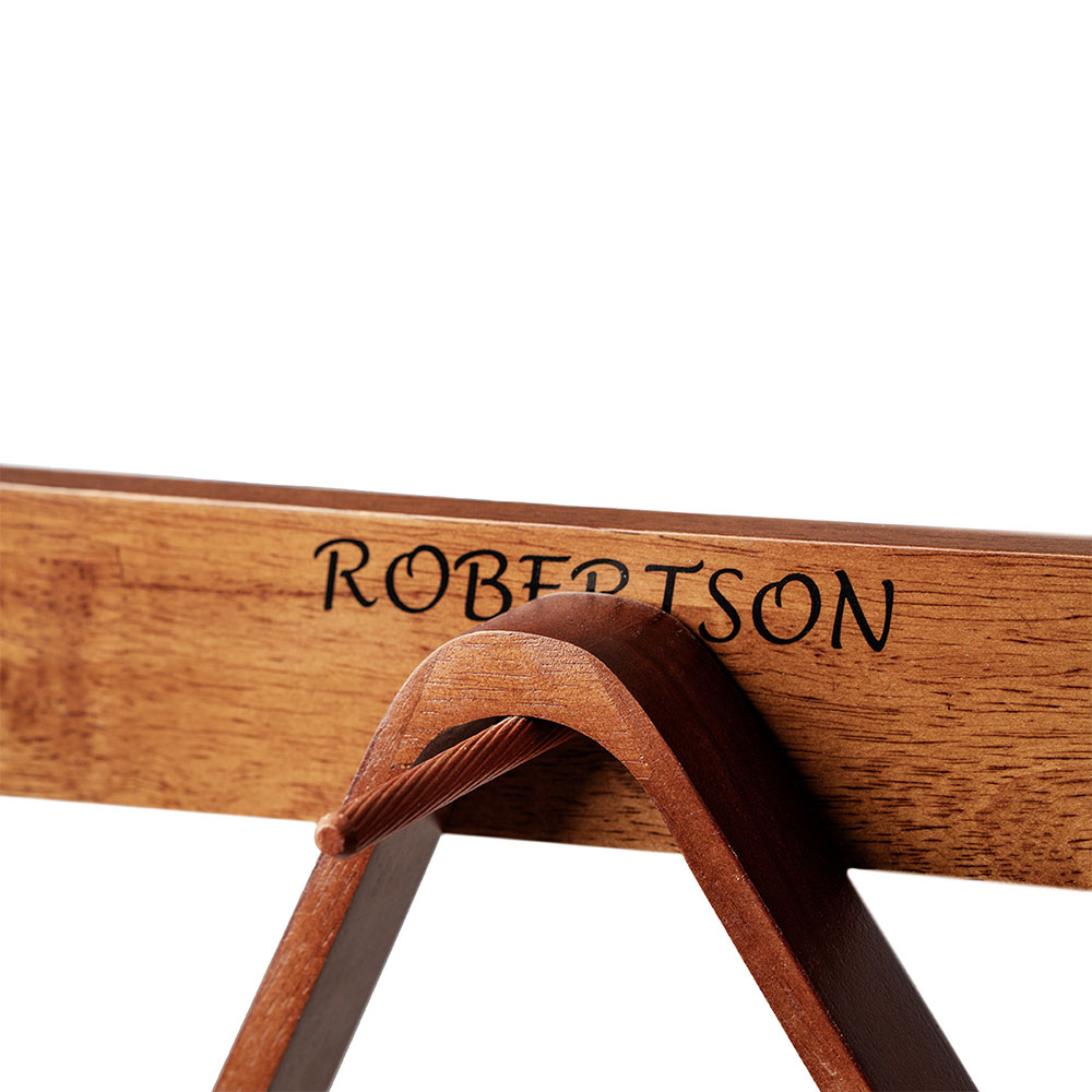 Gros plan sur une planche en bois brun clair portant l'inscription « Robertson » en lettres noires et courbes. En dessous, un étrier en bois brun foncé courbé, traversé par une corde torsadée de couleur brun rougeâtre. Fond blanc.