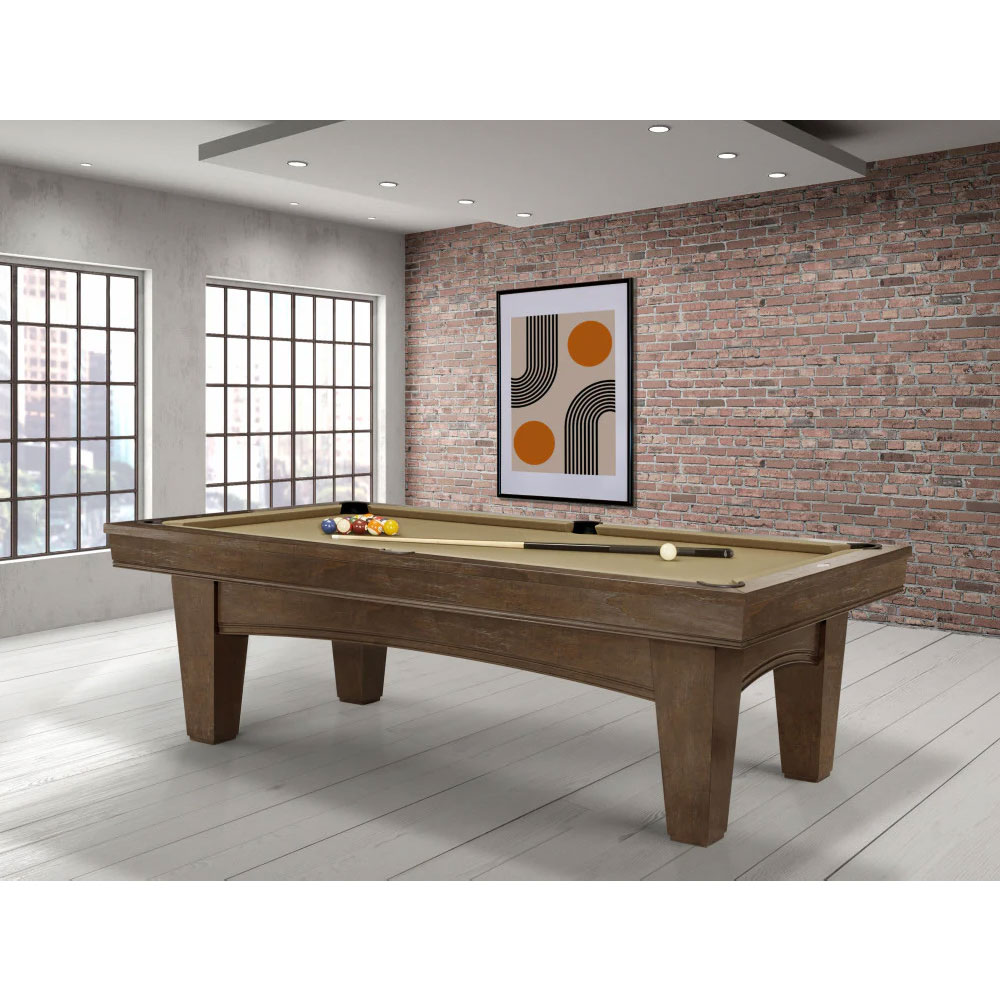 Brunswick ’s modern Winfield pool table with a nutmeg finish and a light-coloured playing surface. Colourful pool balls, a white cue ball and a cue are provided. An 8ft table in a room with a brick wall and large windows.
