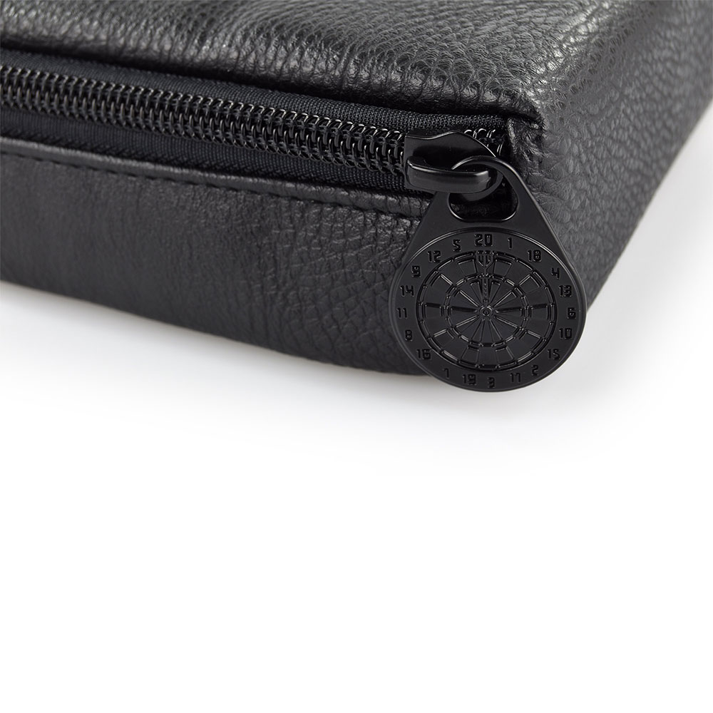 Close-up of the top section of a black, grained leather dart case. A black zip runs along the top edge. The zip pull features a small, round black emblem resembling a dartboard with numbered segments.
