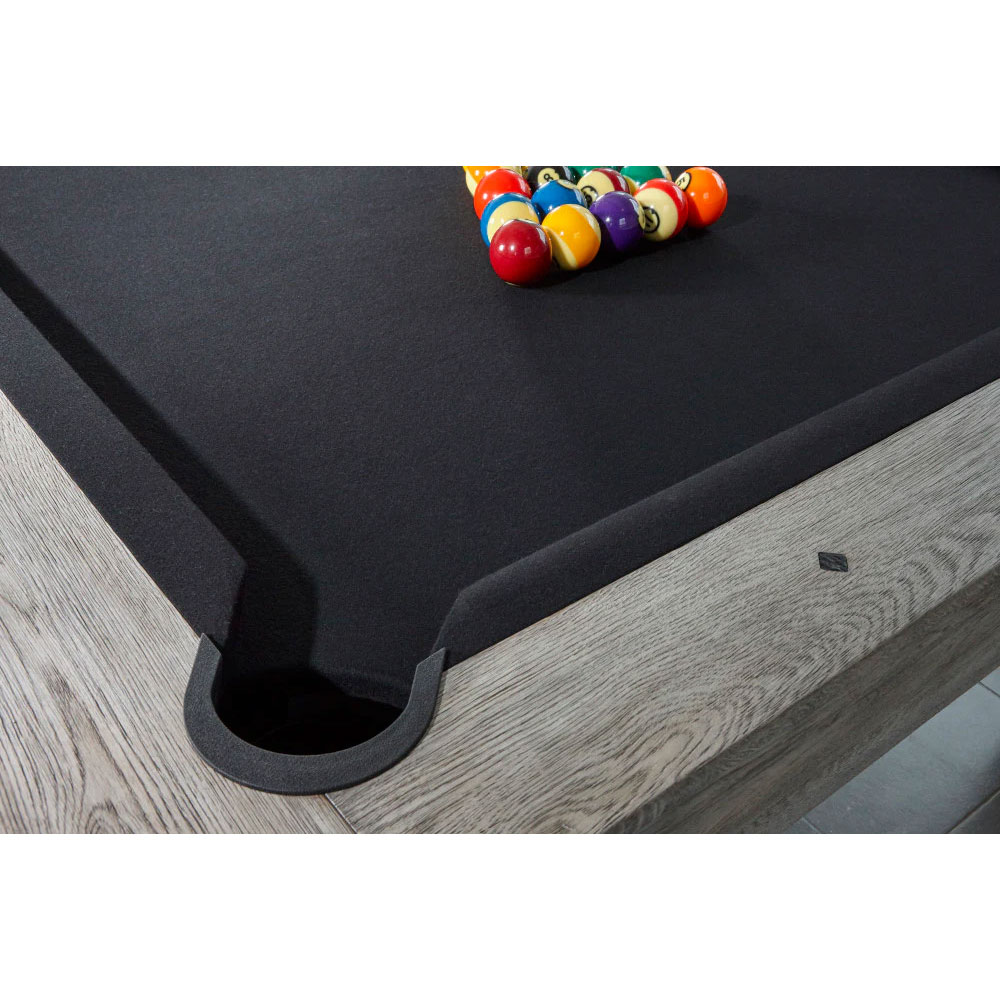 Brunswick 's modern Sanibel pool table with dark cloth and rustic grey wood grain on the rails. Colourful billiard balls are arranged in a triangle on the playing surface. A flush-mounted corner pocket is visible.