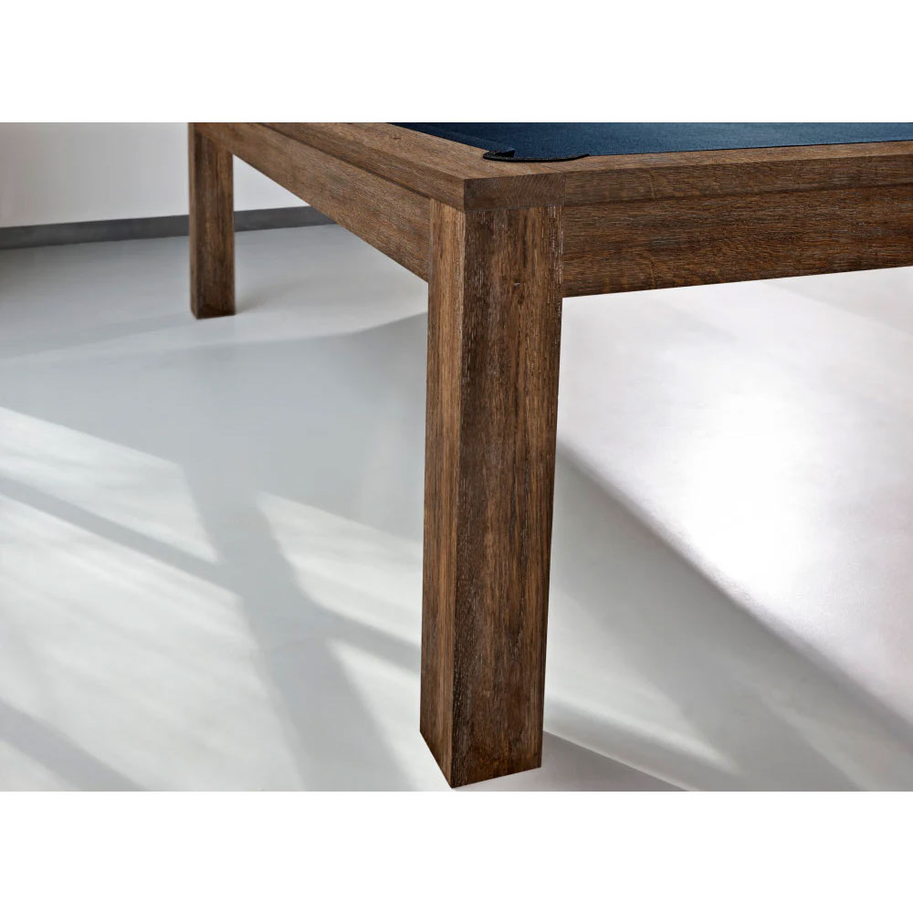 Gros plan sur un coin de la table de billard moderne Soho d'Brunswick, avec une finition noisette. Les pieds en bois massif, de forme carrée, présentent un grain brun foncé. Une partie de la surface de jeu bleu foncé est visible en haut.