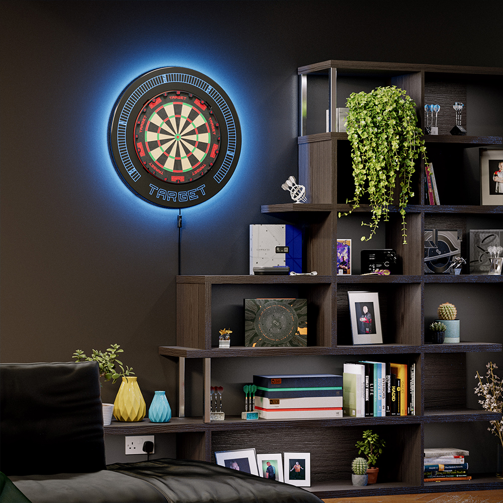 Une cible de fléchettes dotée d’un anneau de capture noir et d’un éclairage d’ambiance LED bleu intégré est accrochée à un mur sombre et baignée d’une lumière bleu clair. À droite se trouve une étagère en bois avec des livres et des plantes.