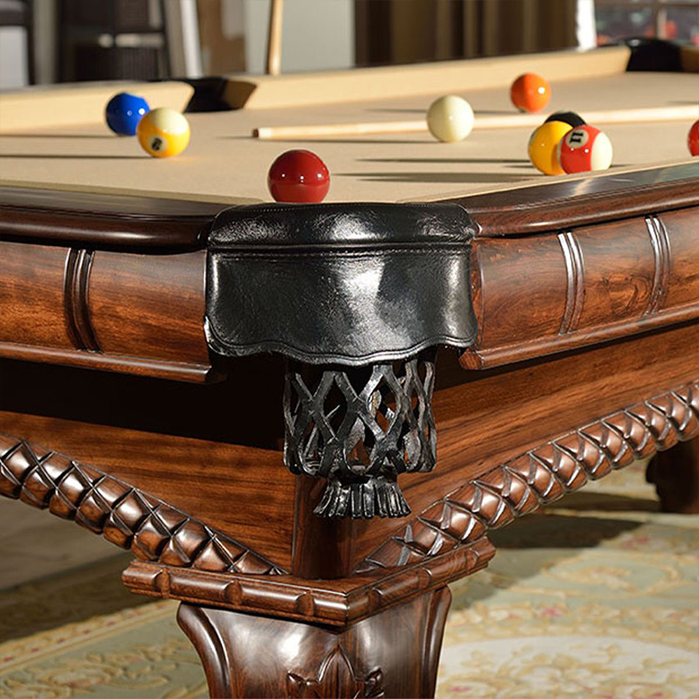Vue détaillée d'une table de billard de luxe « Arizona » avec des sculptures sur bois raffinées et des incrustations au look antique. Une poche d'angle en cuir noir et un filet métallique artistique. Les boules sont prêtes à l'emploi.
