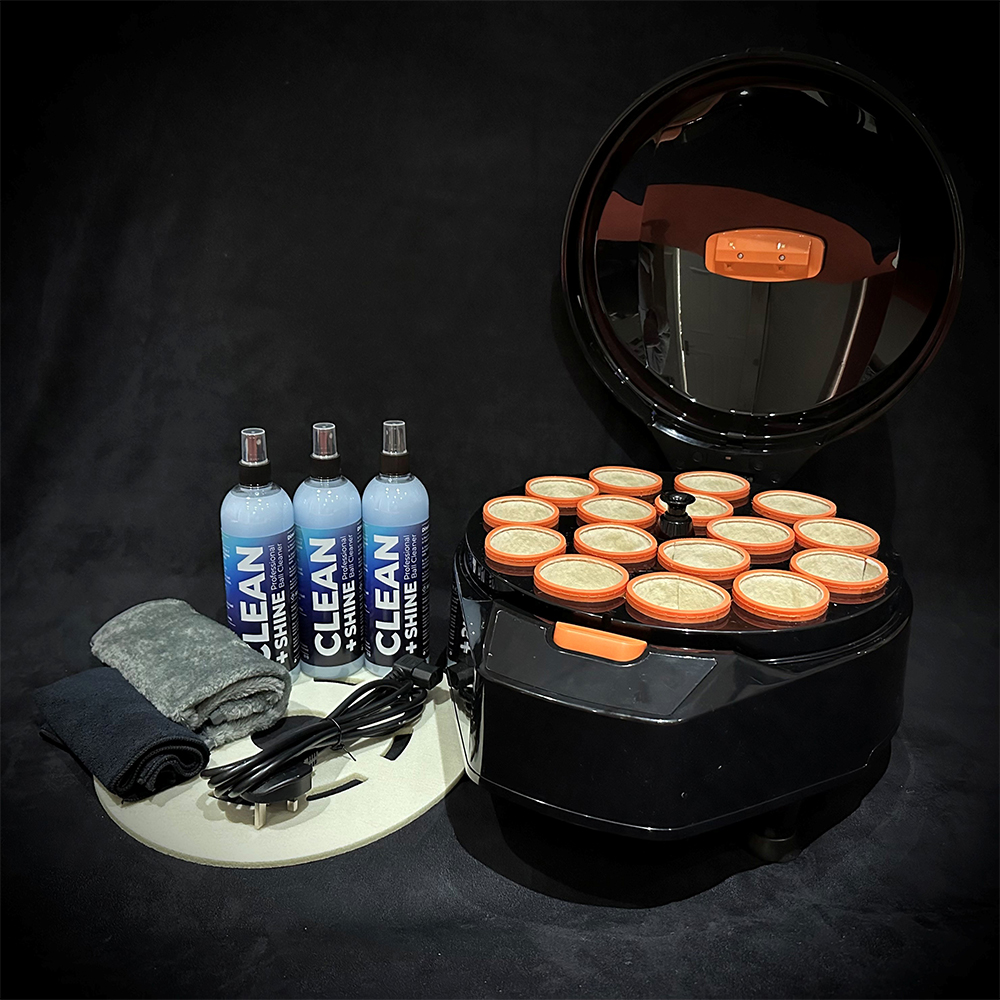 Machine à polir les boules de billard noire avec couvercle ouvert et 16 godets de nettoyage bordés d'orange. À côté : 3 flacons bleus « Clean & Shine », 2 chiffons roulés (gris/noir), un câble d'alimentation et un tampon de rechange.