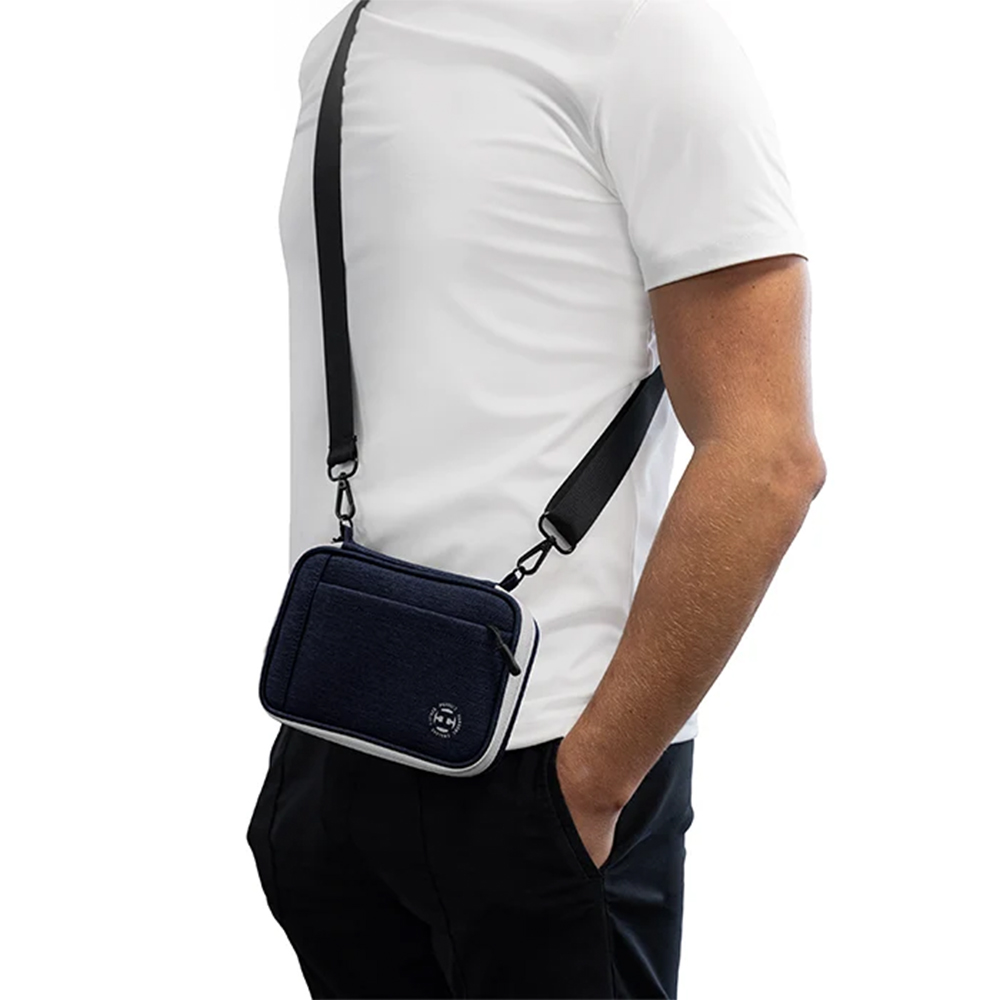Un homme porte en bandoulière sur le torse un étui à fléchettes bleu « Harrows Smart Case XL» bordé de blanc. Cet étui compact en tissu texturé est muni d'une bandoulière noire. Sur le devant, on distingue un compartiment à fermeture éclair et le logo.