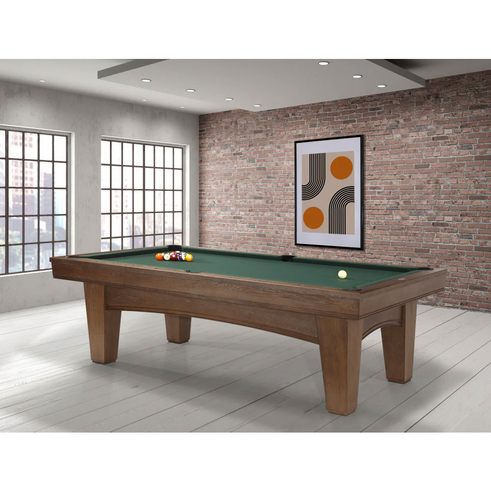 Modern Brunswick Winfield pool table in a nutmeg finish with green cloth in a bright room. 8ft table with a group of balls at the starting point and a white ball. In the background, a window with a view of the city, a brick wall and an abstract painting.