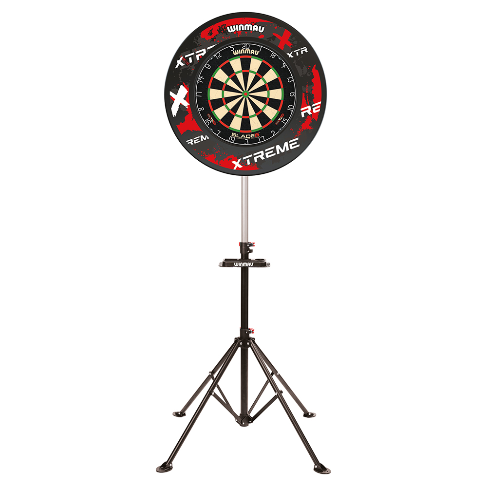 Ein Winmau Blade 6 Dartboard mit schwarzen und roten Segmenten ist mittig auf einem runden, schwarzen Wandschutz mit roten Akzenten und "Xtreme"-Branding montiert. Das Set steht auf einem stabilen, höhenverstellbaren Stativ.