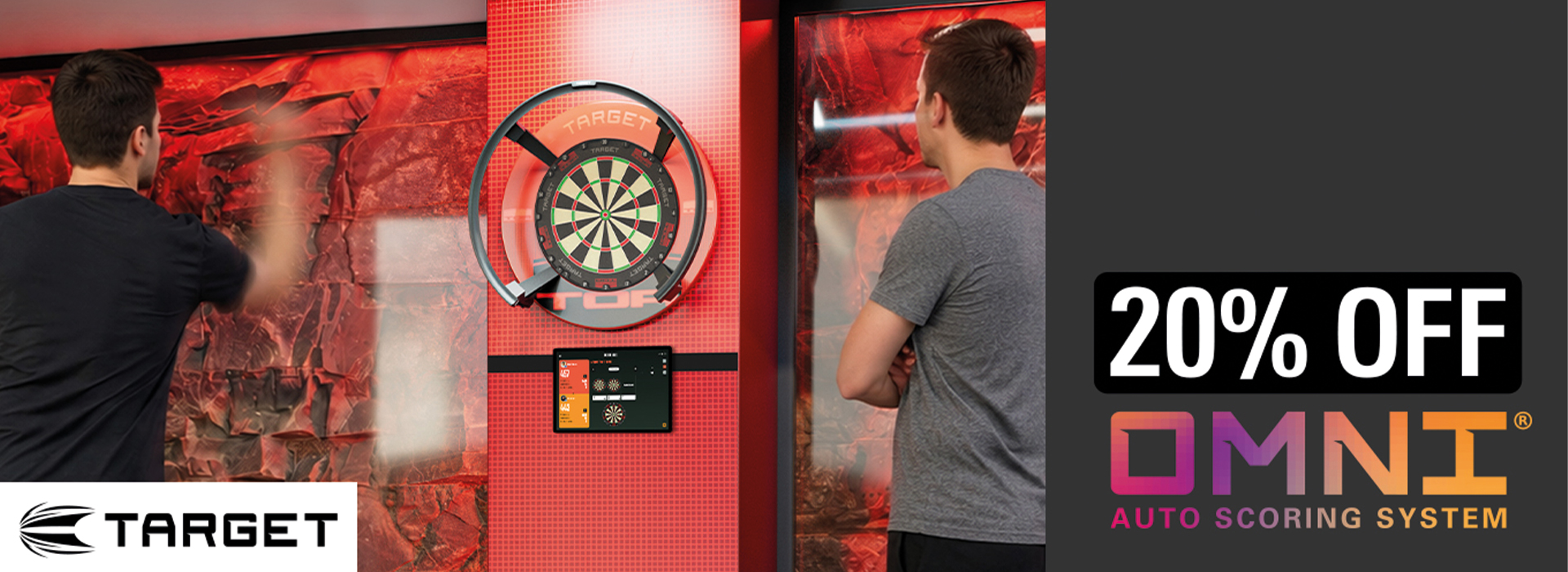 Zwei Männer spielen Darts in einem stilvoll rot beleuchteten Raum. Einer wirft einen Dart auf eine elektronische Dartscheibe, der andere beobachtet. Darunter steht ein Tablet für die Spielanzeige. Die Wände wirken felsartig.