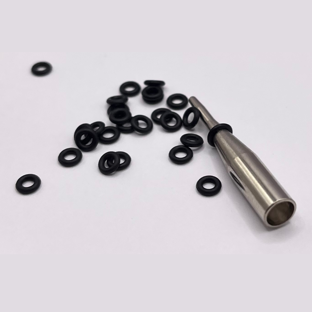 Plusieurs petits joints toriques noirs reposent sur un fond clair. À droite, un outil en aluminium pointu surmonté d'un joint. Ils forment un système de verrouillage pour les tiges 2BA et empêchent celles-ci de se desserrer.