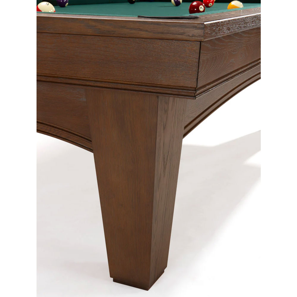 Detailed view of a modern pool table, the Brunswick Winfield, featuring solid, dark wooden legs and a frame in a nutmeg finish. Above, the green playing surface with colourful billiard balls, some of which are against the cushion.