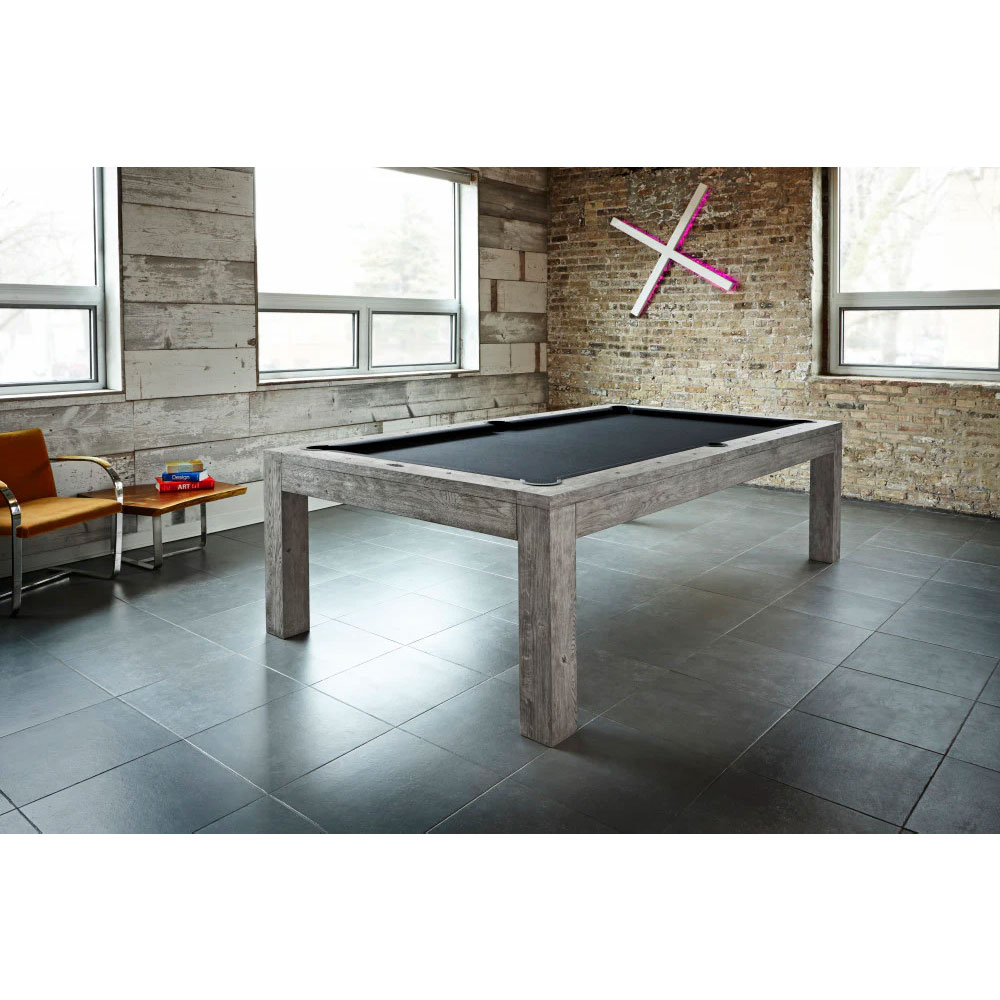 Brunswick Sanibel 8ft pool table in Rustic Grey. Weathered wood finish with visible grain, black baize and flush-mounted pockets. Situated in a modern room with large windows and wood and brick walls.