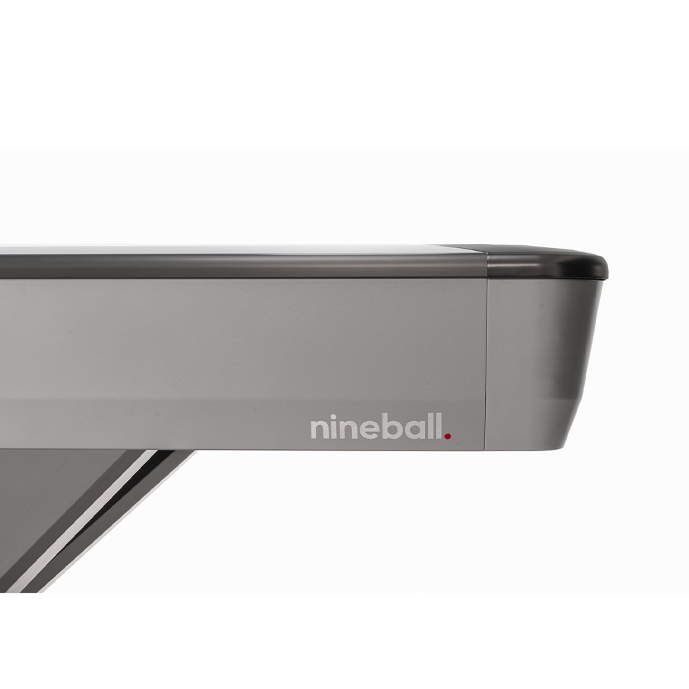 Vue détaillée du coin supérieur d'une table de billard Rasson Victory III argentée. Panneau latéral lisse et argenté avec un bord foncé et un coin arrondi noir. « nineball. » avec un point rouge. Partie du pied en V.