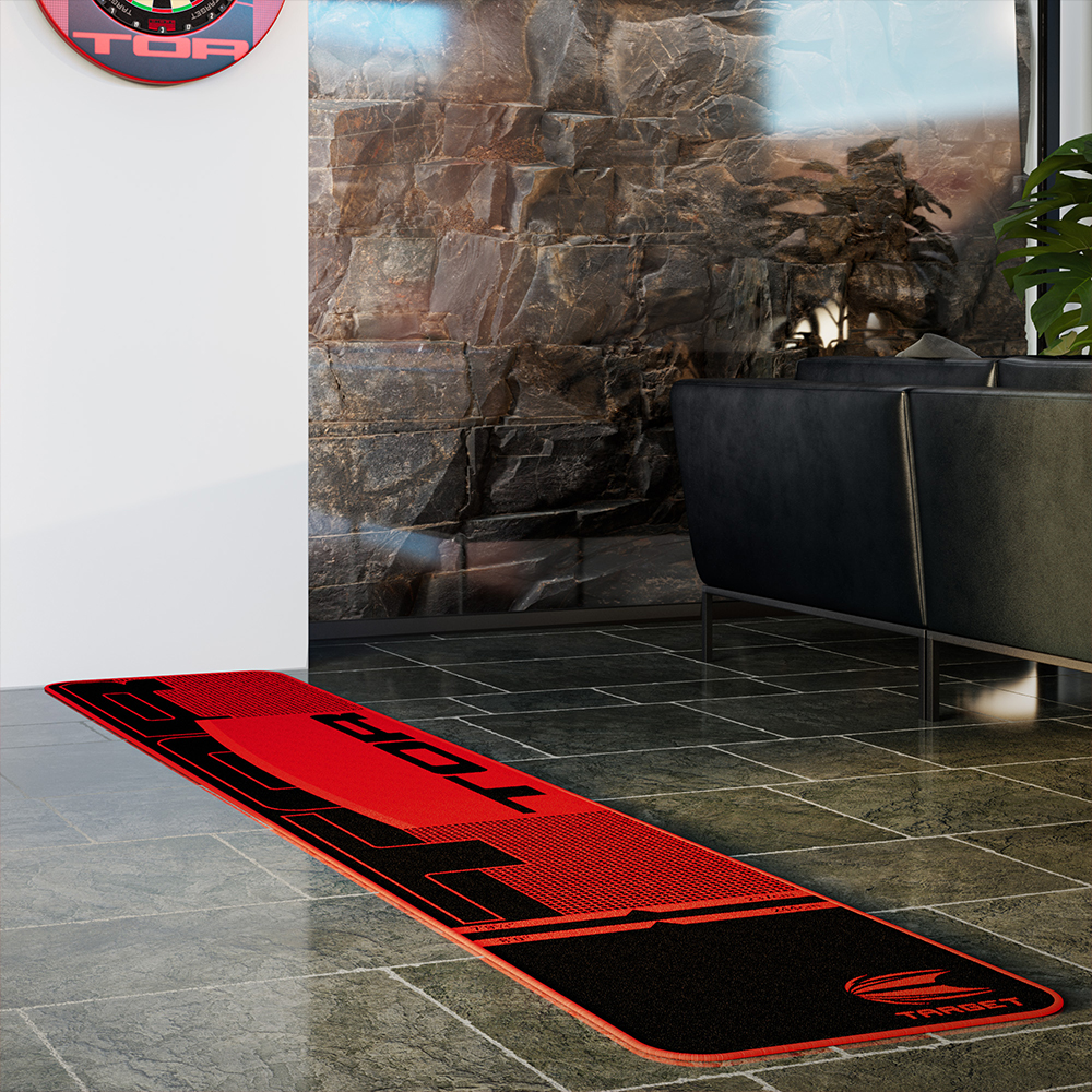 Long tapis de fléchettes noir « Target » TOR sur carrelage foncé, centre rouge et grand « TOR ». Lignes de tir blanches. En arrière-plan : mur en pierre, canapé noir et cible TOR rouge/noire sur mur blanc.
