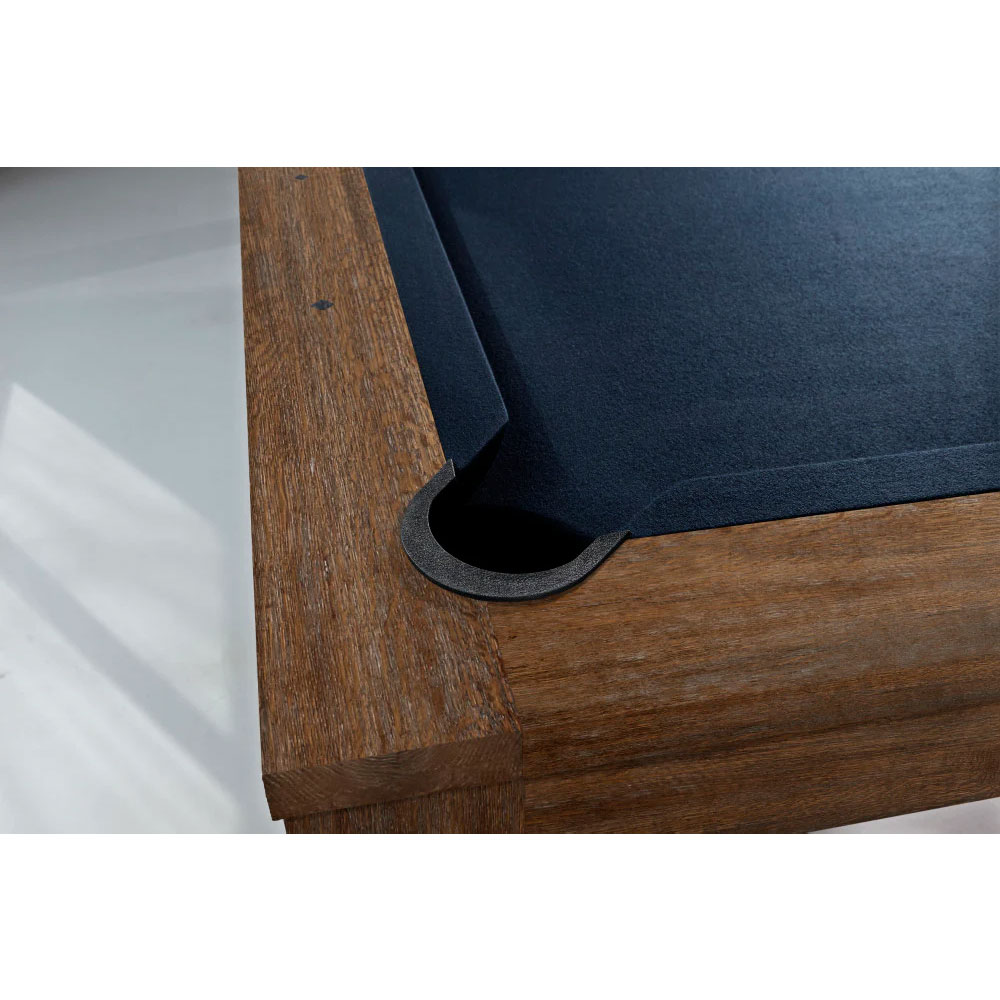 Gros plan sur un coin d'une table de billard moderne « Brunswick Soho » en noyer. Surface de jeu en feutre bleu foncé, poches noires à encastrement plat. Piètement en bois massif avec veinage et détails martelés à la main.