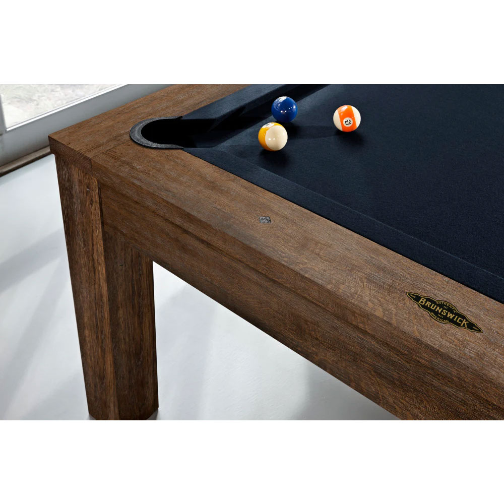 Table de billard moderne « Brunswick » Soho, finition noix de muscade, avec un corps en bois foncé et un tapis bleu foncé. Poche encastrée visible, à côté de laquelle se trouvent trois boules : une bleue, une rayée de jaune et une rayée d'orange (n° 12).