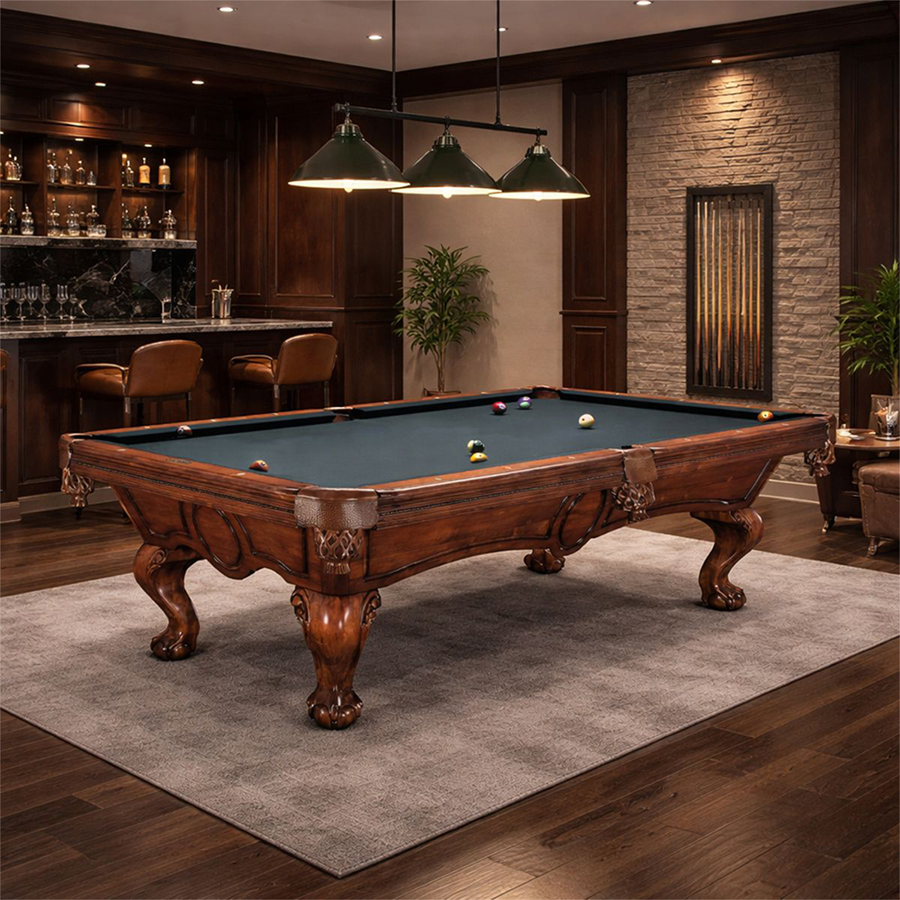Salle de jeux premium avec table de billard en bois foncé, feutre vert, quelques boules, éclairée par trois suspensions. À gauche, bar avec bouteilles et tabourets ; à droite, mur en pierre avec porte-queues.
