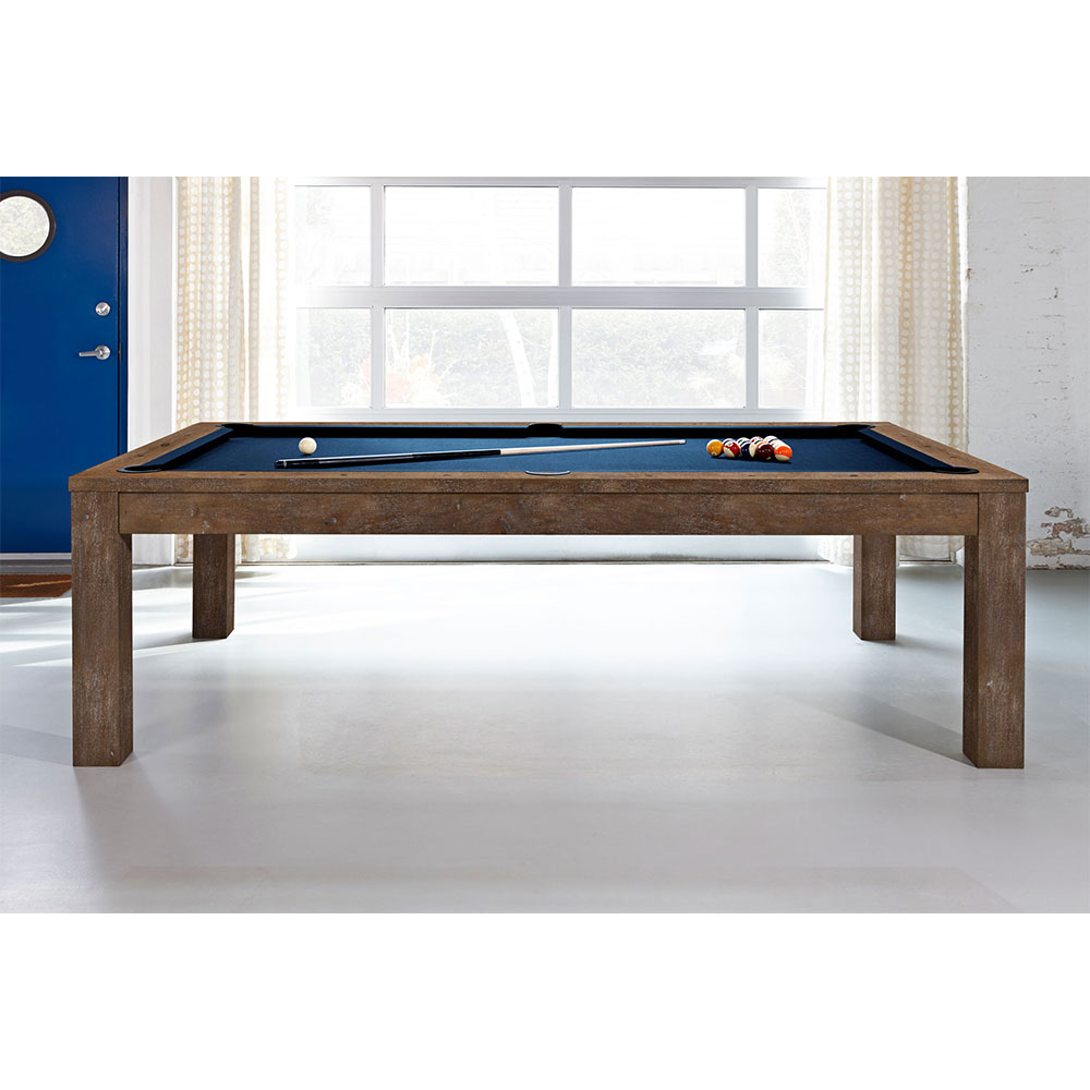 Table de billard moderne « Brunswick » Soho, finition noisette, avec tapis bleu foncé. Sur le tapis, une boule blanche, une queue et des boules de couleur. 8 pieds, design élancé, poches plates, pieds massifs. Fenêtre en arrière-plan.